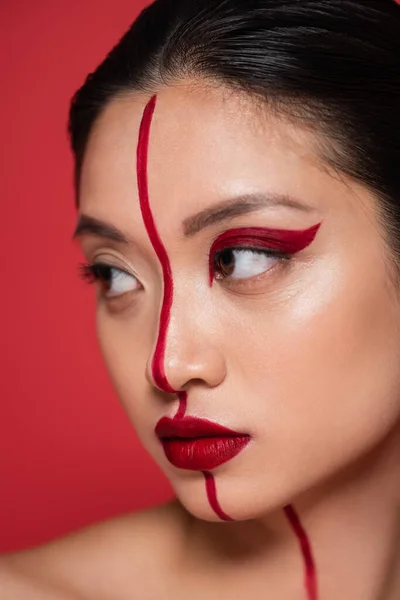 Close up portrait of pretty asian woman with creative visage on face divided with line isolated on red — Stock Photo