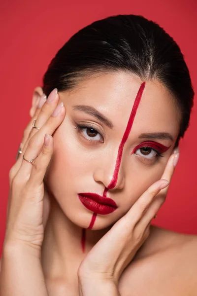 Porträt einer asiatischen Frau, die Gesicht mit perfekter Haut und künstlerischem Aussehen berührt, isoliert auf Rot — Stock Photo