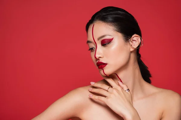 Morena mujer asiática con maquillaje creativo y puño de oreja posando con hombros desnudos aislados en rojo — Stock Photo