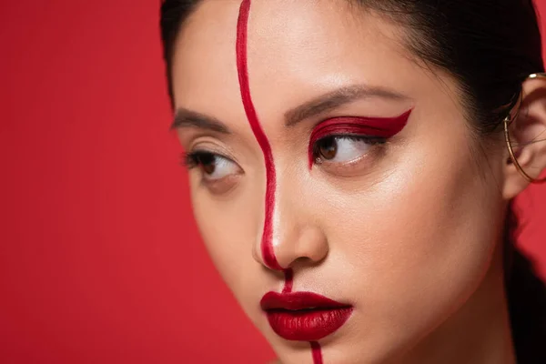 Nahaufnahme Porträt einer asiatischen Frau mit artistischem Make-up im Gesicht geteilt mit einer Linie isoliert auf Rot — Stockfoto