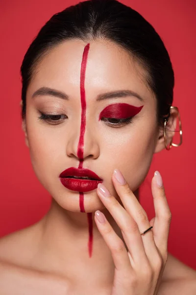 Retrato de joven asiático mujer artístico maquillaje y oreja manguito tocar cara aislado en rojo - foto de stock