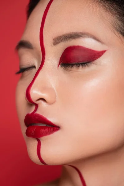 Close up retrato de mulher asiática com olhos fechados e visagem criativa no rosto dividido com linha isolada no vermelho — Fotografia de Stock
