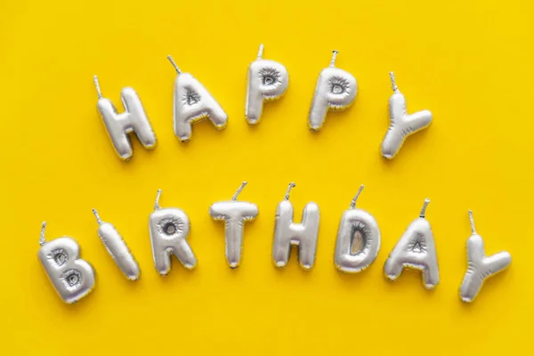 Vista superior de las velas festivas en forma de letras de Feliz Cumpleaños sobre fondo amarillo - foto de stock
