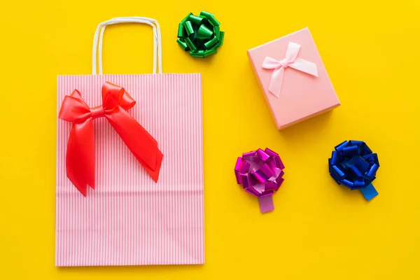 Top view of shopping bag and gift bows near present on yellow background — Stock Photo