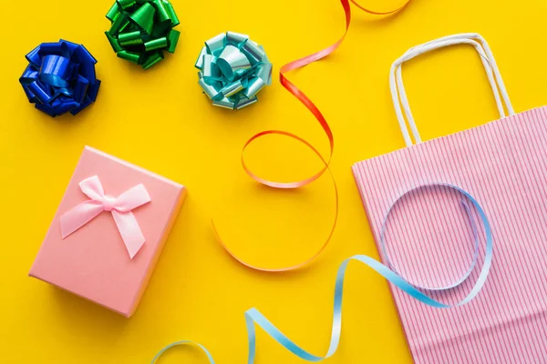 Top view of gift bows near present and shopping bag on yellow background — Stock Photo