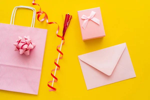 Top view of pink envelope near present and shopping bag on yellow background — Stock Photo