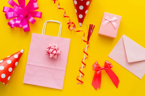 Top view of gift box near party caps and shopping bag on yellow background — Stock Photo
