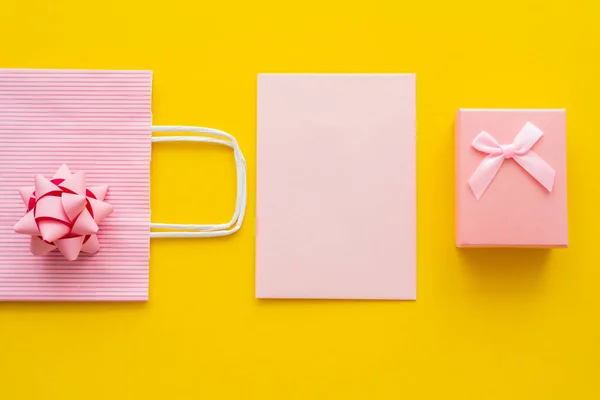 Вид сверху розового подарка рядом с пустой поздравительной открыткой и сумкой для покупок на желтом фоне — стоковое фото