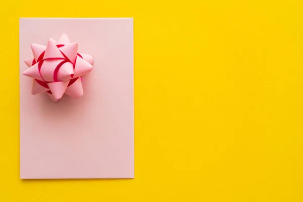 Top view of pink greeting card with gift bow on yellow background with copy space — Stock Photo
