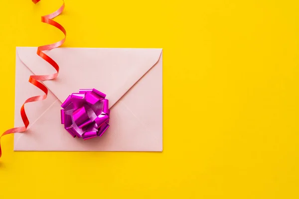 Top view of envelope and gift bow near serpentine on yellow background — Stock Photo