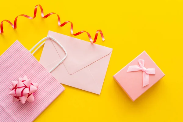 Top view of pink shopping bag near envelope and present on yellow background — Stock Photo