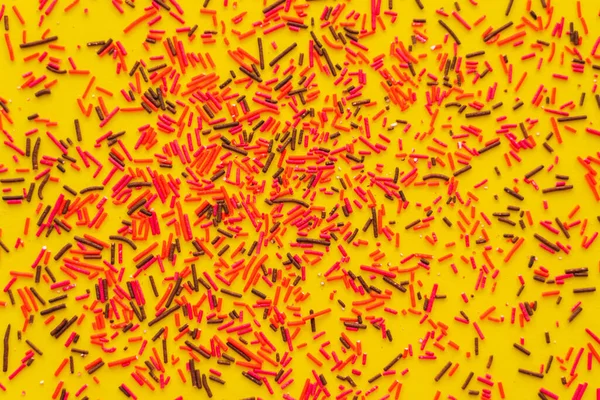 Top view of red and black sweet sprinkles on yellow background — Stock Photo