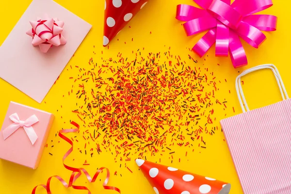 Top view of festive gift near party caps and sprinkles on yellow background — Stock Photo
