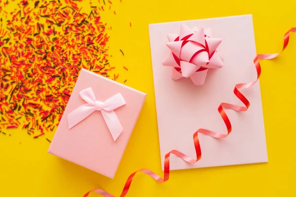 Vue du dessus du cadeau festif et de la carte de vœux près des taches floues sur fond jaune — Photo de stock