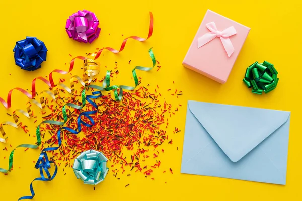 Top view of envelope near gift and sweet sprinkles on yellow background — Stock Photo