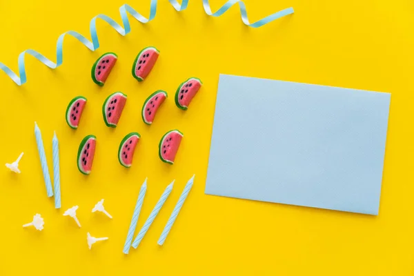 Вид на конфеты возле праздничных свечей и поздравительная открытка на желтом фоне — стоковое фото