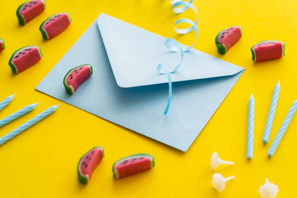 Umschlag in der Nähe von festlichen Kerzen und Süßigkeiten auf gelbem Hintergrund — Stockfoto