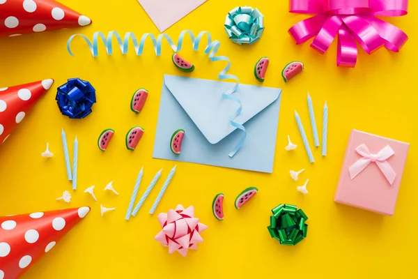 Top view of present near envelope and party caps on yellow background — Stock Photo