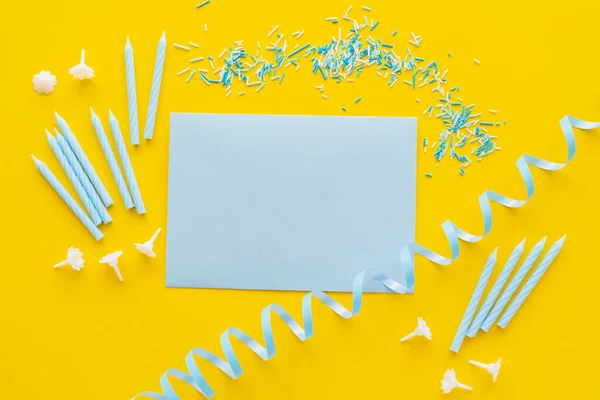 Top view of empty greeting card near candles and blue serpentine on yellow background — Stock Photo