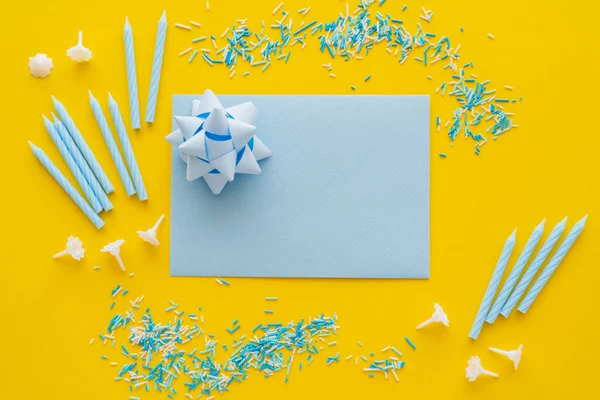 Верхний вид поздравительной открытки с подарочным луком и синими свечами на желтом фоне — стоковое фото