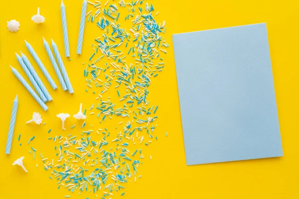 Top view of empty blue greeting card near sprinkles and candles on yellow background — Stock Photo
