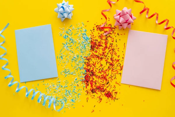 Top view of blue and pink greeting cards near sprinkles and serpentine on yellow background — Stock Photo