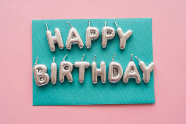 Vista superior de las velas en forma de letras de Feliz Cumpleaños en la tarjeta sobre fondo rosa - foto de stock