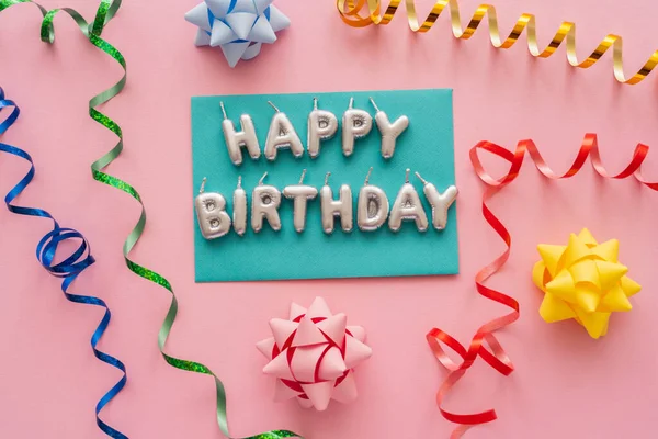 Vista dall'alto delle candele a forma di Happy Birthday lettering vicino alla serpentina e fiocchi regalo su sfondo rosa — Foto stock