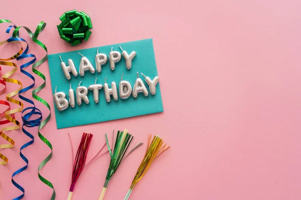 Vista dall'alto di candele a forma di Buon compleanno lettering vicino serpentino e cannucce da bere su sfondo rosa — Foto stock