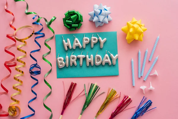 Top view of festive candles in shape of Happy Birthday lettering near serpentine and drinking straws on pink background — Stock Photo