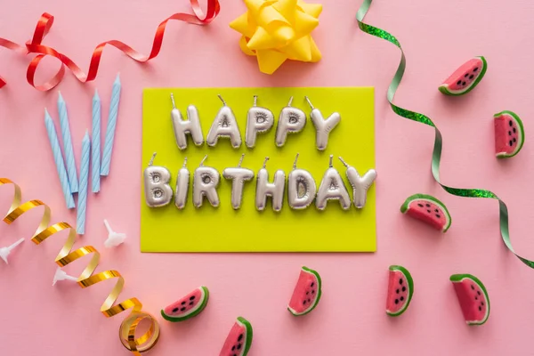 Top view of candles in shape of Happy Birthday lettering near sweets and serpentine on pink background — Stock Photo