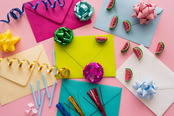Vista superior de envelopes coloridos perto de doces e serpentina em fundo rosa — Fotografia de Stock