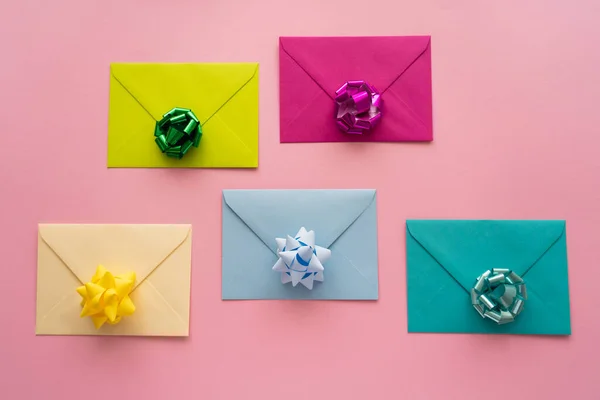 Vue du dessus des noeuds cadeaux colorés sur des enveloppes sur fond rose — Photo de stock