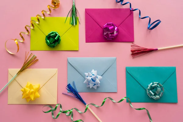 Top view of colorful gift bows on envelopes near serpentine on pink background — Stock Photo