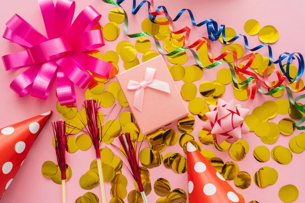Vue du dessus du présent sur confettis près des chapeaux de fête et serpentine sur fond rose — Photo de stock