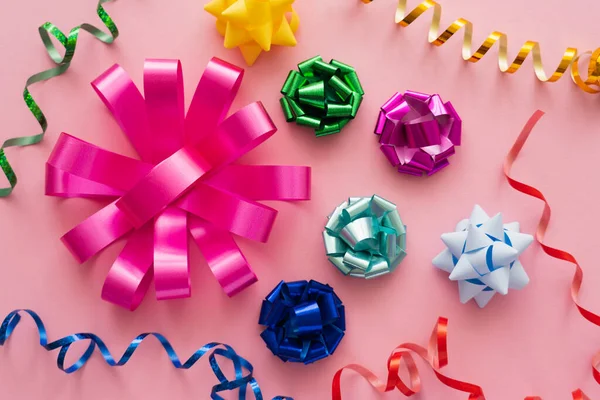 Draufsicht auf bunte Geschenkbögen und Serpentinen auf rosa Hintergrund — Stockfoto
