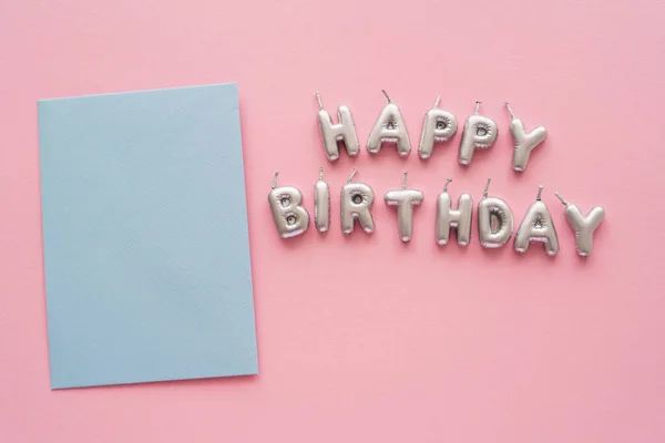 Top view of greeting card near candles in shape of Happy Birthday lettering on pink background — Stock Photo