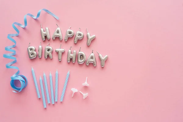 Vue du dessus des bougies en forme de lettrage Joyeux anniversaire près de serpentine bleue sur fond rose — Photo de stock