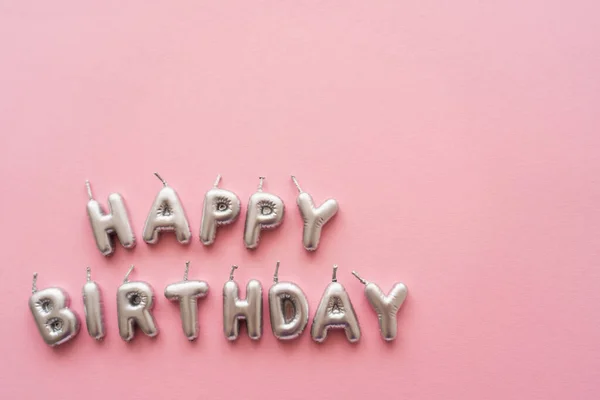 Vista superior de velas de plata en forma de letras de Feliz Cumpleaños sobre fondo rosa - foto de stock