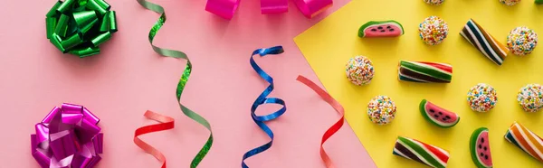 Vue du dessus des bonbons près de noeuds cadeaux colorés et serpentine sur fond rose, bannière — Photo de stock