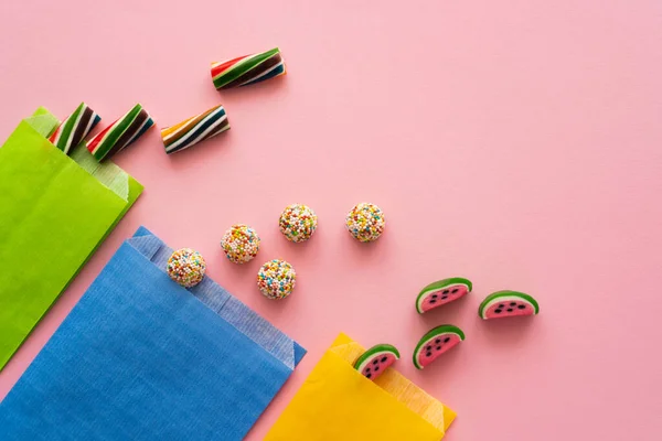 Vista superior de dulces caramelos y bolsas de papel sobre fondo rosa - foto de stock