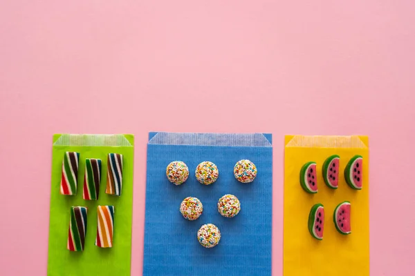 Vista superior de diferentes caramelos en bolsas de papel de colores sobre fondo rosa - foto de stock