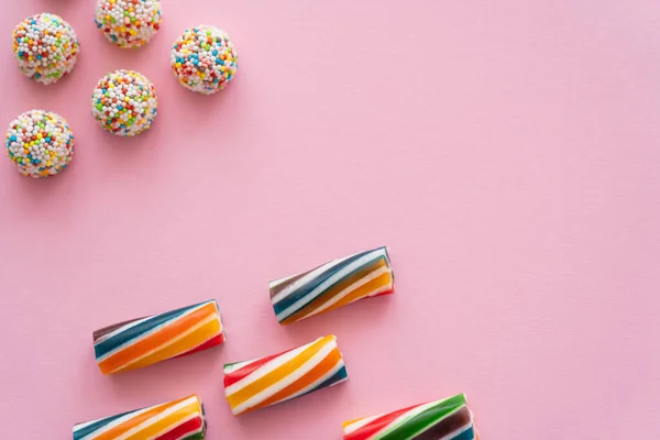 Flache Lage mit gestreiften und bunten Bonbons auf rosa Hintergrund — Stockfoto