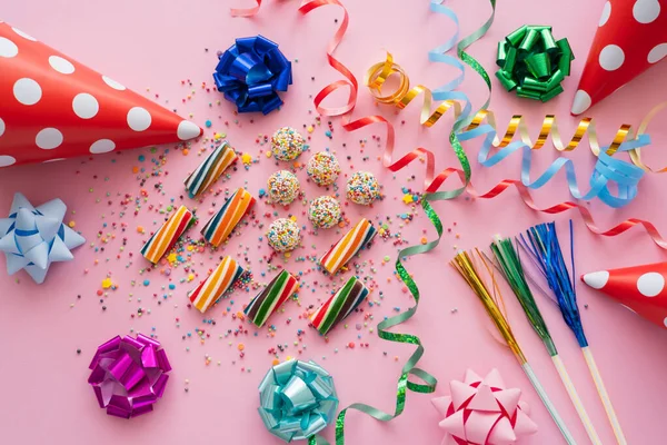 Vue du dessus de bonbons colorés près de serpentine et casquettes de fête sur fond rose — Photo de stock