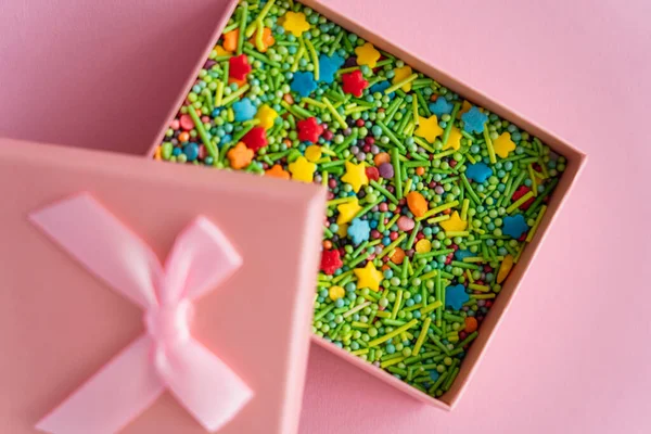 Vista superior de polvilhas coloridas na caixa de presente no fundo rosa — Fotografia de Stock