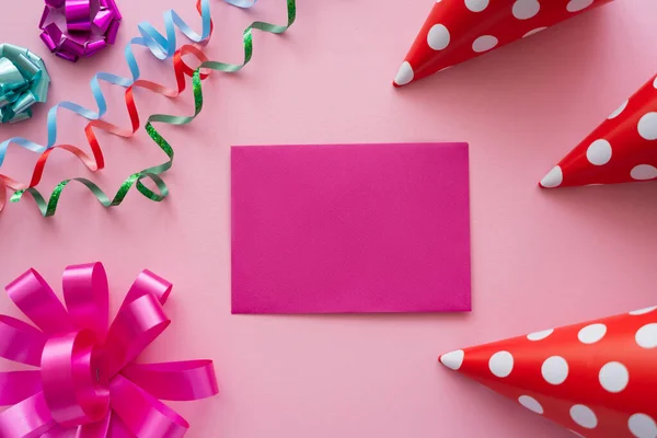 Top view of empty greeting card near serpentine and party caps on pink background — Stock Photo