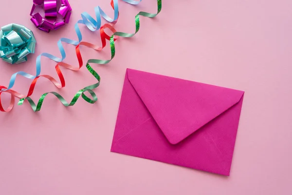 Top view of envelope near serpentine and gift bows on pink background — Stock Photo