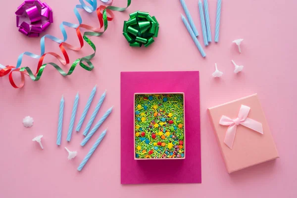 Top view of sprinkles in gift box near candles and serpentine on pink background — Stock Photo