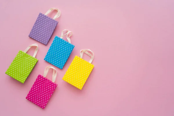 Vista superior de pequeñas bolsas de compras punteadas sobre fondo rosa con espacio para copiar - foto de stock