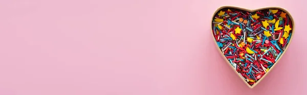Draufsicht auf bunte Streusel in herzförmiger Geschenkbox auf rosa Hintergrund, Banner — Stock Photo